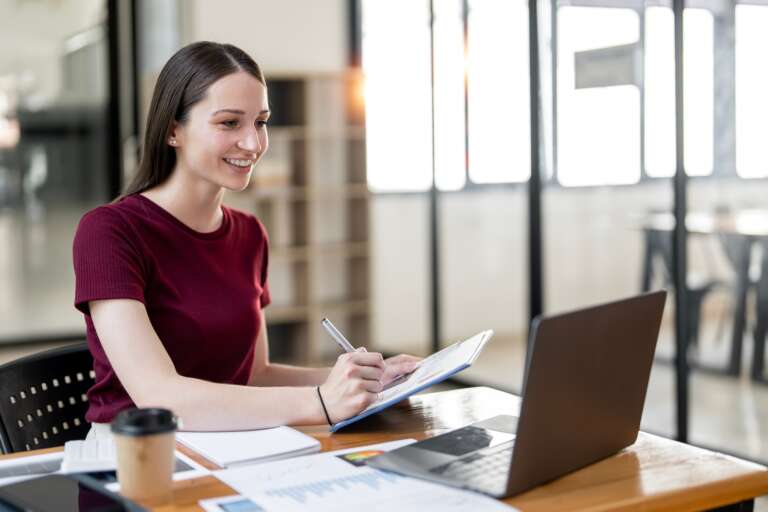 Successful businesswoman using laptop and computer while doing some paperwork at the office.